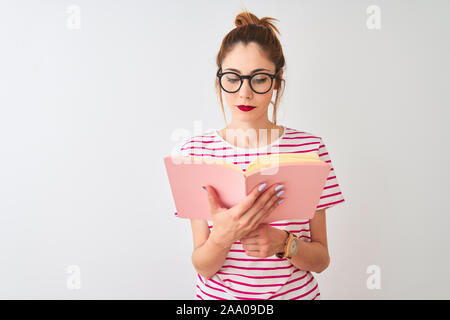 Schöne rothaarige Frau Brille lesen rosa Buch über isolierten weißen Hintergrund mit einem selbstbewussten Ausdruck auf Smart Face denken Ernst Stockfoto