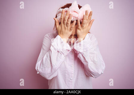 Junge schöne rothaarige Frau in Pyjama stehend über rosa isoliert Hintergrund Kopfschmerzen leiden, verzweifelte und betonte, weil Schmerz und mi Stockfoto
