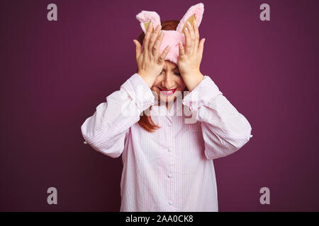 Junge schöne rothaarige Frau in Pyjama und Maske über Violett isolierte Hintergrund Kopfschmerzen leiden, verzweifelte und betonte, weil Schmerz und Stockfoto