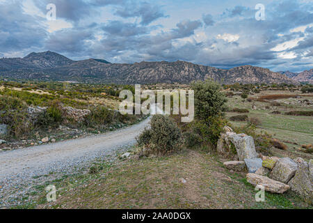 Landschaft mit landwirtschaftlichen Straße Felder mit ihren Hügeln und im Hintergrund die Sierra de Guadarrama ein bewölkter Tag. Madrid Spanien Stockfoto