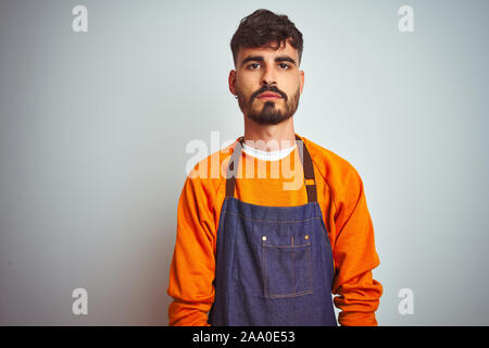 Junge Ladenbesitzer Mann mit Tattoo tragen Schürze stehend über isoliert weißer Hintergrund mit ernsten Gesichtsausdruck. Einfache und natürliche auf der Suche Stockfoto