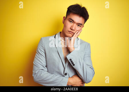 Jungen asiatischen chinesischen Geschäftsmann tragen Jacke stehend über isolierte gelben Hintergrund denken müde und gelangweilt mit Depressionen Probleme mit Stockfoto
