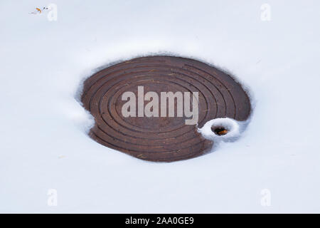 Kanalisation Mannloch auf einer Stadt Bürgersteig bedeckt mit weißen Schnee. Stockfoto