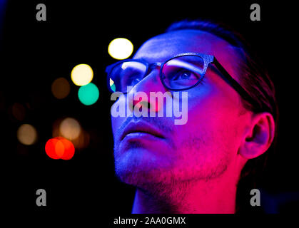 Modernes rotes und blaues Licht Porträt eines jungen Mannes in Gläsern. Straßenbeleuchtung im Hintergrund sichtbar. Stockfoto