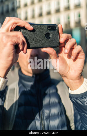 Junger Mann in einem Gap ist ein Foto mit seinem Handy auf der Straße der europäischen Stadt. Stockfoto