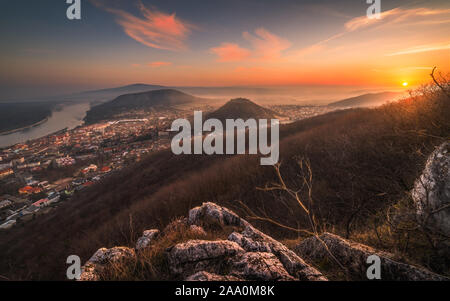 Blick auf eine kleine Stadt in der Nähe von Donau bei Sonnenaufgang. Hainburg an der Donau, Österreich ab dem hundsheimer Berg mit Rocky Vordergrund gesehen. Stockfoto