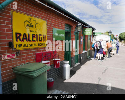 Plattform Isfield Station in East Sussex mit Nebengebäuden in roten Ziegelsteinen mit grünen Türen und eine Anzeige für Raleigh Fahrräder Stockfoto