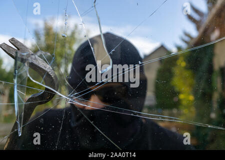 Einbrecher bricht die Fenster. Einbrecher mit Gesicht versuchen, das Fenster zu Bruch verdeckt Stockfoto