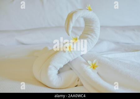 Schönen Schwan von weiße Badetuch auf weißen Bett dekorieren. Handtuch Swan mit aktuellen Blumen - Frangipani. Schönen Gruß vom Hotel. Stockfoto