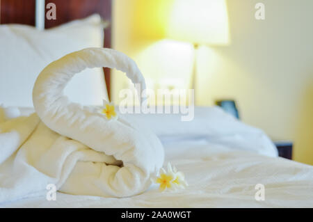 Schönen Schwan von weiße Badetuch auf weißen Bett dekorieren. Handtuch Swan mit aktuellen Blumen - Frangipani. Schönen Gruß vom Hotel. Stockfoto