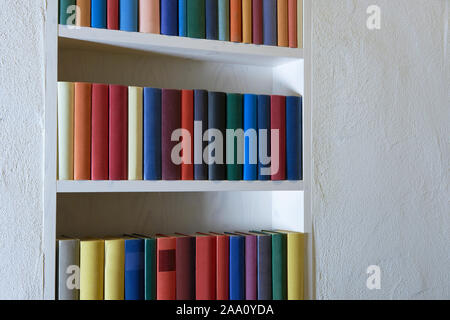 Bunte Bücher in einem Bücherregal in Weiß verputzte Wand Genaue Stockfoto