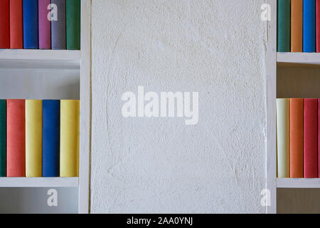 Weiße Wand mit bunten Bücher im Regal Stockfoto