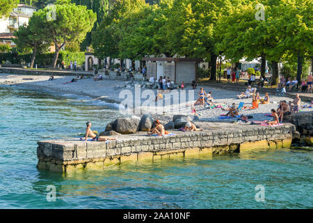 PORTESE, ITALIEN - September 2018: Menschen beim Sonnenbaden auf den steinernen Steg in der Ortschaft Portese am Gardasee. Stockfoto