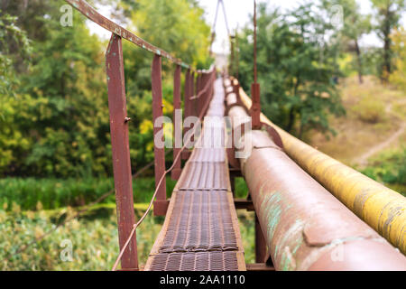 Einen schmalen alten rostigen River Crossing, zusammen mit einer Wasser- und Gasleitung. Kommunikation im Dorf Stockfoto