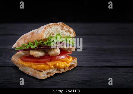 Appetitlich Sandwich auf einem Holzbrett. Baguette Sandwich mit Füllung aus Kopfsalat, Scheiben Tomate. Dunklen Hintergrund. Blick von oben. Close-up. Stockfoto