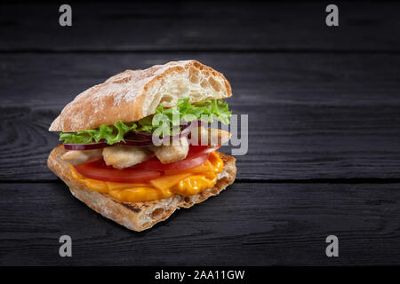 Appetitlich Sandwich auf einem Holzbrett. Baguette Sandwich mit Füllung aus Kopfsalat, Scheiben Tomate. Dunklen Hintergrund. Blick von oben. Close-up. Stockfoto