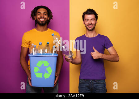 Freunde halten ein Kunststoffbehälter mit Flaschen über Gelb und Violett. Konzept der Ökologie, Umweltschutz, Recycling und Nachhaltigkeit Stockfoto