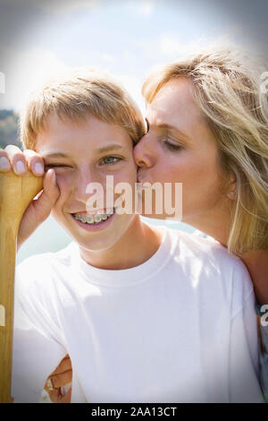 Lächelnd Teenager mit Klammern auf seine Zähne Küssen auf die Wange von seiner Mutter. Stockfoto