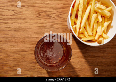 Draufsicht auf das Bier im Glas in der Nähe lecker Pommes frites in Schaufel auf Holz- Hintergrund Stockfoto
