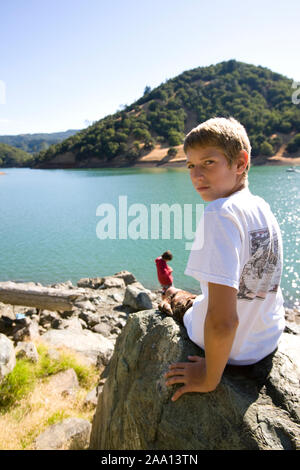 Porträt einer Junge sitzt auf einem Felsen in der Nähe von einem See. Stockfoto