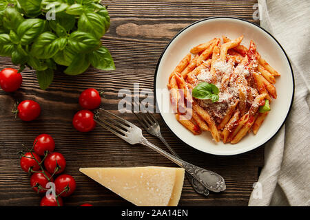 Blick von oben auf die leckere bolognese Nudeln mit Tomatensoße und Parmesan in weiße Platte in der Nähe von Zutaten und Besteck auf hölzernen Tisch Stockfoto