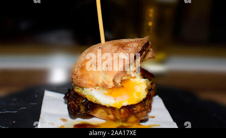 Close up mini Burger mit gegrillten Angus Rindfleisch, Speck, Käse, gebratenen Wachteln Eier und Sahne Saucen auf thecraft Papier und Holz- Hintergrund. Stockfoto