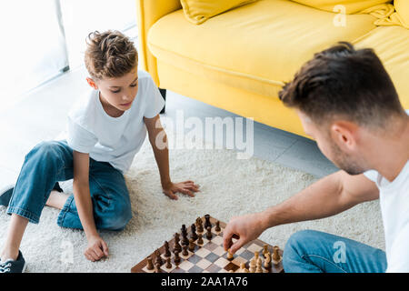 Ansicht von oben von Vater und Sohn spielt Schach auf dem Teppich Stockfoto