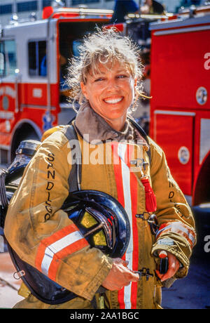 Ihre Sicherheit Mantel tragen und den Helm tragen, eine Frau fire fighter stellt neben ihr Rig in der Innenstadt von San Diego, CA. Stockfoto