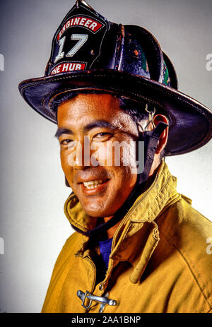 Eine asiatische amerikanische Feuerwehrmann in San Diego, CA, stellt seinen Helm und Sicherheit Kleidung tragen. Die Abzeichen auf seinem Helm zeigt an, er ist ein Fahrer von einem Löschfahrzeug. Stockfoto