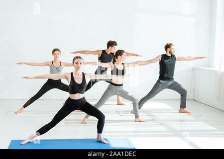 Fünf junge Männer und Frauen Yoga im Krieger II darstellen Stockfoto
