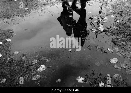 Reflexion in einem regen Pfütze mit gefallenen Blätter im Herbst von zwei Menschen zu Fuß entlang der Promenade am Meer, in der mumbles Swansea South Wales Stockfoto