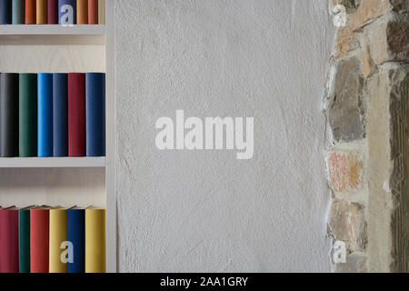 Weiße Wand in einem Loft mit Teil von Bücherregal mit bunten Bücher und ein Teil der Mauer aus Stein Stockfoto