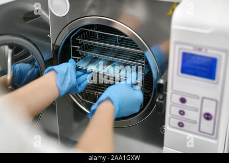 Arzt in blau Latex Handschuhe ist Einfügen versiegelt Zahnärztliche Sonden in einem Autoklav Sterilisator. Closeup horizontale Foto. Stockfoto