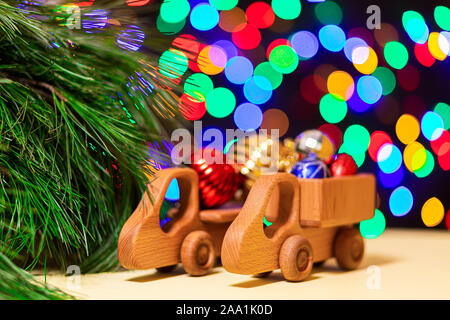 Close-up 2 Holz Spielzeug-LKW brachten bunten Weihnachtskugeln zu einem Weihnachtsbaum auf dem Hintergrund der vielen bunten Lichtern. Bild für das Neue Jahr des Stockfoto