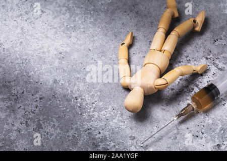 Eine Spritze mit Drogen und daneben liegt die Abbildung eines Mannes aus Holz. Süchtiger auf dem Boden. Konzept zum Thema Drogen Entzug mit Kopie spac Stockfoto