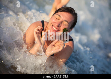 Das Gesicht einer alten Frau in die Wellen des Meeres. Ältere Frau am Strand. Porträt einer älteren Frau baden im Meer Stockfoto