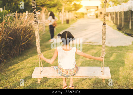 Zurück Blick auf junge Mädchen auf Schaukel sitzen für Ihre Mutter in der biologisch angebauten Trauben Bauernhof warten. Stockfoto