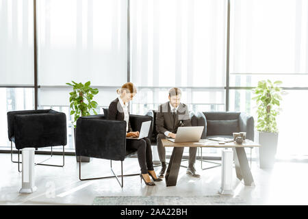 Angestellte von Finanzinstituten arbeiten mit Laptops in der luxuriösen Büro, sitzen auf dem bequemen Sofa in der Nähe der grossen Fenster Stockfoto