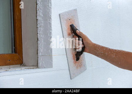 Hand eines Arbeitnehmers mit einem Werkzeug zum Schleifen und Glätten und sogar die Oberfläche einer Hauswand mit Styrofoam Dämmplatten isoliert. Stockfoto