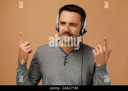 Stattliche emotionale Call Center Mitarbeiter Mann auf beigen Hintergrund isoliert. Junge Customer service agent mit Headset und emotional über die Vorteile eines Produktes. Stockfoto