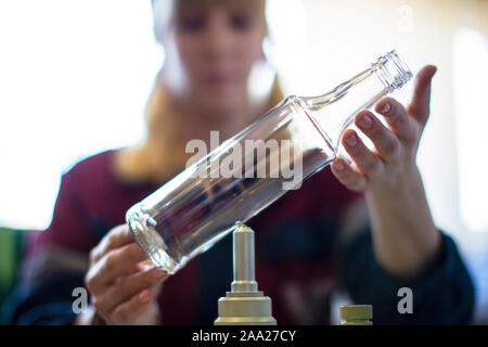 Belarus, die Stadt von Gomil, 2. Oktober 2019. Glashütte. Weibliche Arbeitnehmer hält ein Glas Flasche über das Gerät. Stockfoto