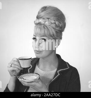 Kaffee in den 1960er Jahren. Eine Frau trinkt Kaffee aus einer Kaffeetasse mit einem 1960er Streifenmuster. Sie hat ihr Haar in den typischen Bienenstock Frisur, in denen lange Haare auf dem Kopf aufgetürmt ist und eine gewisse Ähnlichkeit mit der Form eines traditionellen Bienenstock. Schweden 1962. Ref BV 97-8 Stockfoto