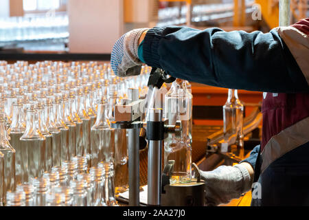 Glashütte. Glasindustrie. Die Hände halten eine Glasflasche auf dem Hintergrund eines Förderbandes. Stockfoto