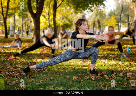 Große Gruppe von Menschen mit Trainer stretching auf grünem Gras in Park Stockfoto
