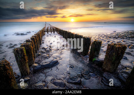 Wellenbrecher aus Holzplatten auf einem Strand bei stürmischem Wetter mit Sonnenuntergang an der Küste von Zeeland, Niederlande Stockfoto