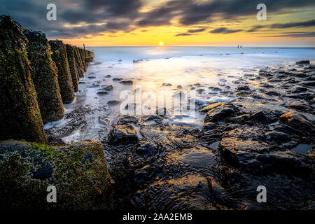 Wellenbrecher aus Holzplatten auf einem Strand bei stürmischem Wetter mit Sonnenuntergang an der Küste von Zeeland, Niederlande Stockfoto