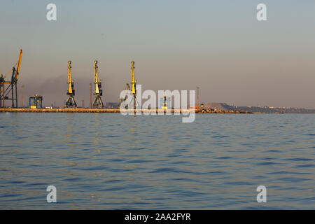 Viele große Kräne Silhouette in den Hafen des Asowschen Meeres im goldenen Licht des Sonnenuntergangs. Mariupol, Region Donetsk, Ukraine Stockfoto