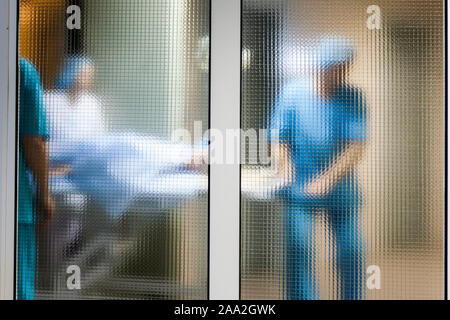 Weibliche Patienten, der von einer Gruppe von Ärzten in einem Krankenhaus OP-Saal auf einem gurney für Herzchirurgie transportiert Stockfoto