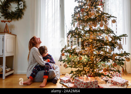 Mutter und Sohn neben einem Weihnachtsbaum kuscheln Stockfoto