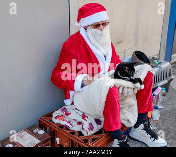 Mann in Santa Kostüm gekleidet sitzt auf Fahrbahn in Oxford Street mit schwarzen und weißen Katze auf seinem Schoß, Weihnachten. Die Oxford Street, London, UK Stockfoto